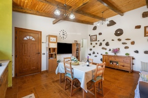 A dining area with a wooden table, chairs, a clock, and a stone wall.