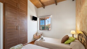 Un dormitorio con dos camas, armario de madera, televisor, ventana con vistas y lámpara de noche.