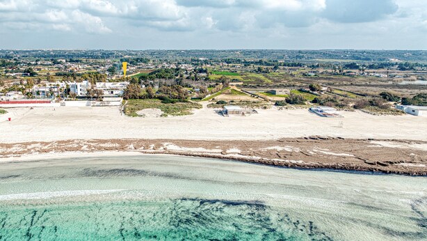 An aerial view of a coastal area with clear turquoise waters, sandy beaches, and scattered buildings. - Holiday Home 'Luce Sulla Spiaggia' with Private Garden and Air Conditioning (Torre San Giovanni)