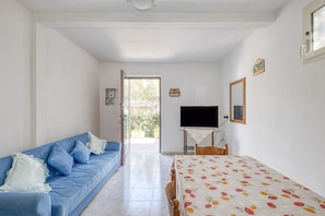 A room with a blue sofa, a table with a floral tablecloth, a television, and a door leading outside. - Holiday Home 'Luce Sulla Spiaggia' with Private Garden and Air Conditioning (Torre San Giovanni)