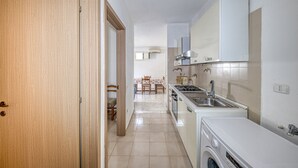 A kitchen with a washing machine, a sink, and a dining area with chairs. - Holiday Home 'Luce Sulla Spiaggia' with Private Garden and Air Conditioning (Torre San Giovanni)