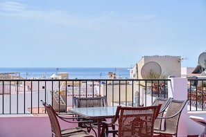 A balcony with wicker furniture, a glass table, and a view of the sea.