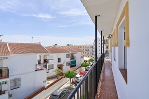 A residential building with a tiled roof, balconies, and a narrow street with parked cars.