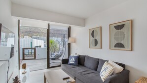 A modern living room with a grey sofa, a coffee table, and a view of a balcony with a hanging chair. - Vacation Apartment 'Sun and Serenity Pool Wifi' with Sea View, Wi-Fi and Air Conditioning (Puerto Rico)