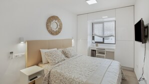 A bedroom with a bed, bedside table, wall-mounted TV, and a desk with a chair. - Vacation Apartment 'Sun and Serenity Pool Wifi' with Sea View, Wi-Fi and Air Conditioning (Puerto Rico)