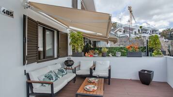 A balcony with a sofa, chairs, a table, and potted plants.