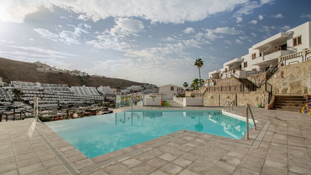 A swimming pool with a view of a hillside and a building with balconies. - Vacation Apartment 'Sun and Serenity Pool Wifi' with Sea View, Wi-Fi and Air Conditioning (Puerto Rico)