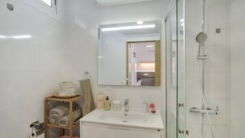 A bathroom with a sink, mirror, shower, and towel rack.