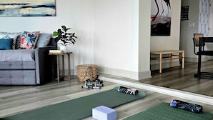 Un salon avec un canapé gris, des tapis de sport verts, une petite table avec une plante et un mur orné d’un tableau.
