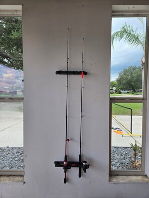 A fishing rod rack mounted on a wall with a view of a parking lot and trees outside.