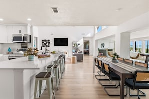 A modern kitchen with a central island, bar stools, and a dining area with a long table and chairs.