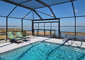 Zona de piscina con vista al agua, sillas de descanso y una terraza cubierta.