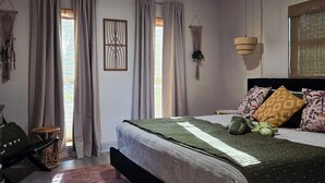 Une chambre à coucher comprenant un lit, un ventilateur de plafond, une fenêtre avec des rideaux, une plante fixée au mur et une table de chevet.