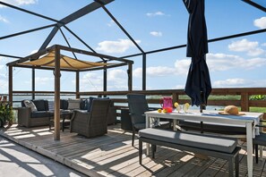 Een houten terras met buitenmeubilair, een tafel met drankjes en uitzicht op het water.