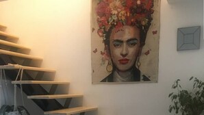 Eine Wendeltreppe mit Holzstufen führt zu einer oberen Etage, ein weißes, fellüberzogenes Sessel, ein gewebter Korb und ein Blumentopf.
