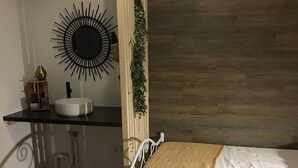 Ein Schlafzimmer mit einem Bett, einem Nachttisch mit einer weißen Ablage, einem Zier-Spiegel und einem Holz-Kopfteil.