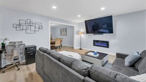 Ein modernes Wohnzimmer mit grauem Sofa, Couchtisch, Wandfernseher und Schreibtisch mit Stuhl.