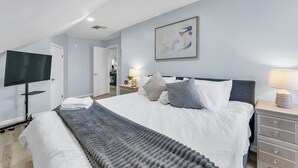 Ein modernes Hotelzimmer mit einem großen Bett, einem Flachbildfernseher, einem Nachttisch mit Lampe und einem Bild an der Wand.