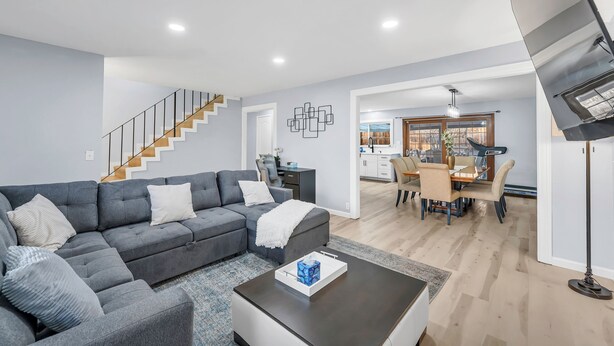 Ein modernes Wohnzimmer mit einem grauen Ecksofa, einem Couchtisch und einer Treppe, die zu einer oberen Etage führt.