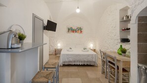 Ein kleiner, gemütlicher Raum mit Bett, Schreibtisch, Stuhl, Fernseher und einem Regal mit Pflanzen.