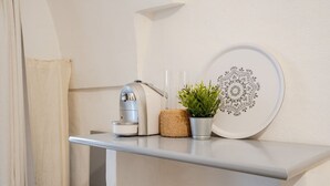 Eine Kaffeemaschine, ein Blumentopf und ein dekoratives Teller auf einem weißen Regal.