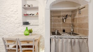 Eine Küche mit gefliestem Rückspritzschutz, einem Spülbecken und einem hängenden Gestell. Es gibt einen Holztisch mit Stühlen und einem grünen Blumenvasen.