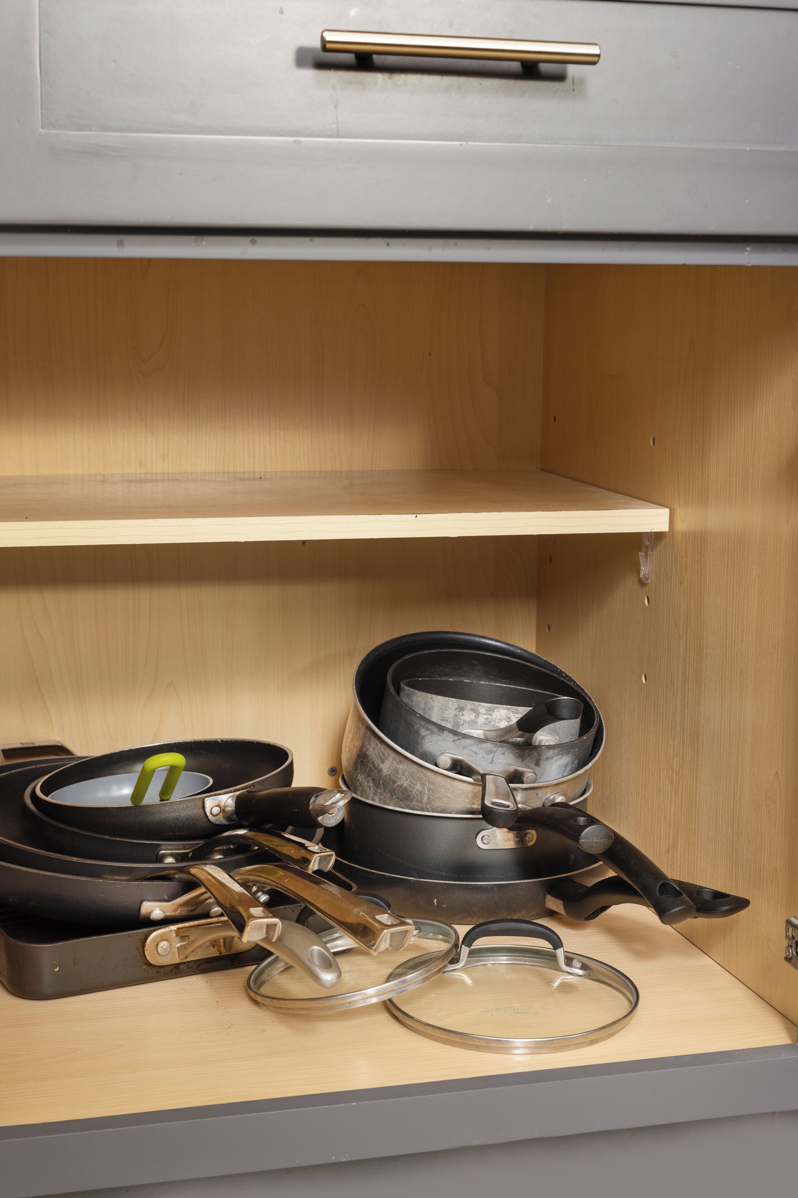 A kitchen cabinet with a drawer and a shelf. The drawer contains a pot, a pan, and a lid. The shelf has a pot and a pan.