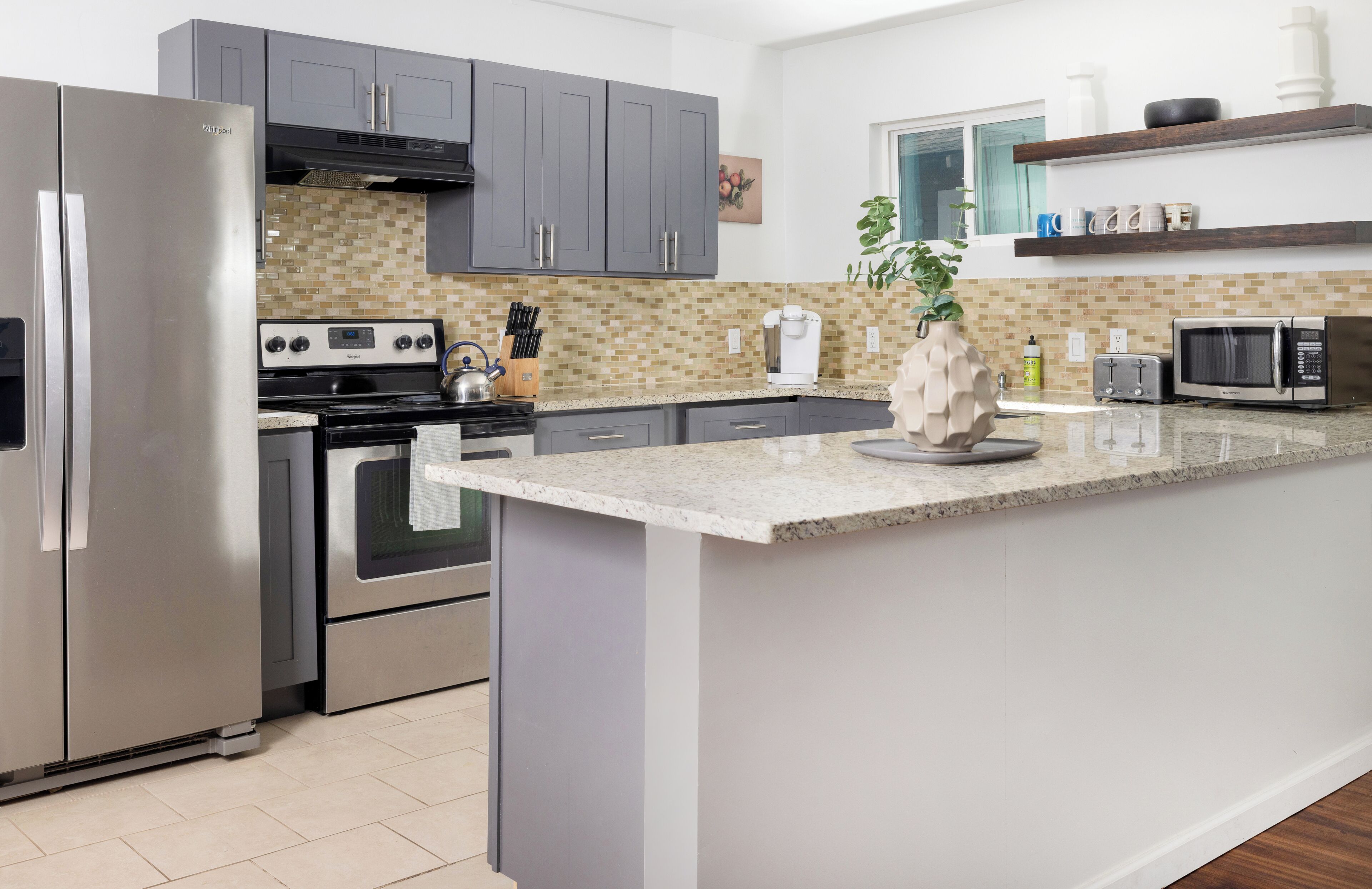 A modern kitchen with grey cabinets, stainless steel appliances, and a granite countertop.