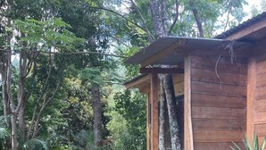 Een houten hut met een veranda, omringd door weelderige begroeiing en bomen.