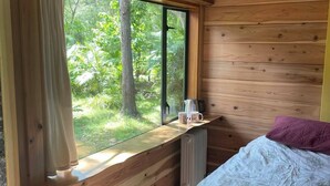 Een houten kamer met een bed, een raam met uitzicht op groen en een radiator.