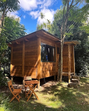Una cabaña de madera con ventana, una pequeña terraza y una silla plegable.
