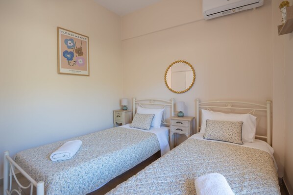 Un dormitorio con dos camas, un cuadro enmarcado en la pared, un espejo redondo y un pequeño florero con flores.