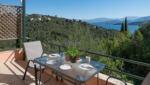 Un balcón con una mesa dispuesta para dos, con vistas a un paisaje montañoso y un cuerpo de agua.