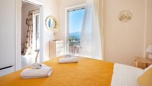 Habitación de hotel con cama, ventana con vistas, cómoda de madera y baño visible a través de una puerta abierta.