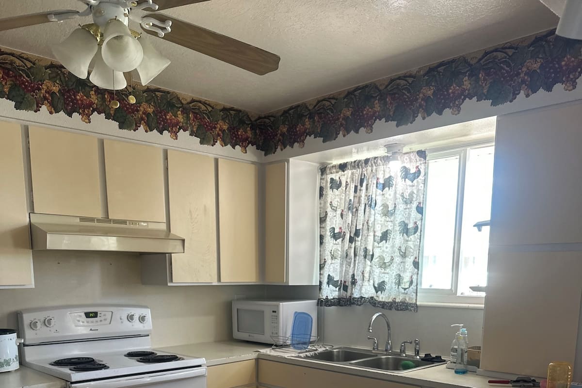 Una cocina con estufa, microondas, fregadero y ventana con cortinas.