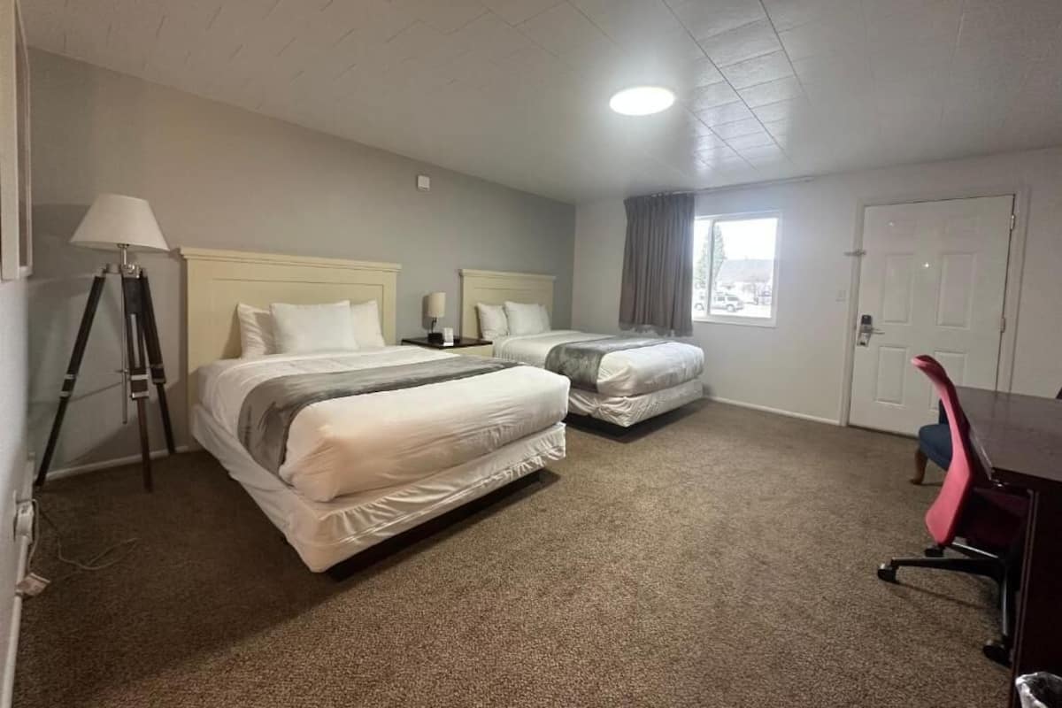 Habitación de hotel con dos camas, un escritorio, una silla, una lámpara y una ventana.