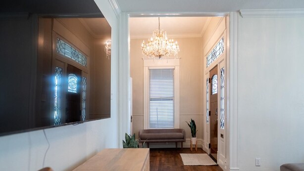 A hallway with a wooden floor, a bench, a chandelier, and a door with stained glass.