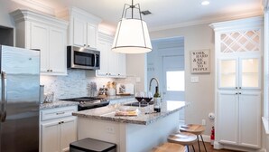 A modern kitchen with white cabinetry, a stainless steel refrigerator, a built-in microwave, and a large island with stools.