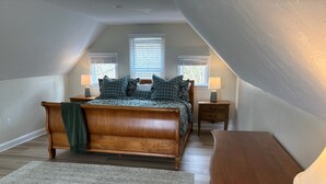A bedroom with a wooden bed, two bedside tables with lamps, a large window, and a view of trees. - New to the market 4BR Cape Cod charmer on Hamblin Pond w Waquoit Bay views (Mashpee)