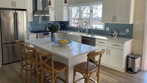 A modern kitchen with a central island, stainless steel appliances, and a view of the outdoors. - New to the market 4BR Cape Cod charmer on Hamblin Pond w Waquoit Bay views (Mashpee)