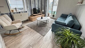 Una sala de estar con sofá, una mecedora, una mesa de centro y un televisor sobre un mueble de madera.