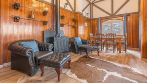 A cozy living room with leather sofas, a fireplace, wooden walls, and a dining area with chairs and a table. - Sierra Nevada Mountains Apartment ‘Edificio Los Alayos’ (Sierra Nevada)