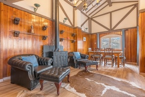 A cozy living room with leather sofas, a fireplace, wooden walls, and a dining area with chairs and a table.