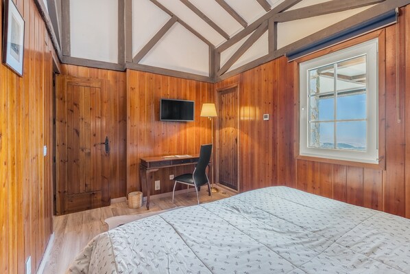 A wooden-paneled room with a bed, desk, chair, and a TV.