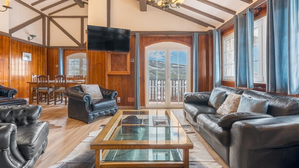 A spacious living room with a glass coffee table, leather sofas, wooden flooring, a dining area, and a large window with a view. - Sierra Nevada Mountains Apartment ‘Edificio Los Alayos’ (Sierra Nevada)