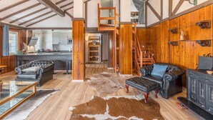A spacious living area with a high ceiling, wooden beams, a staircase, leather furniture, and a kitchen in the background. - Sierra Nevada Mountains Apartment ‘Edificio Los Alayos’ (Sierra Nevada)
