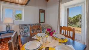 Un comedor con una mesa preparada para cuatro, un sofá, un espejo y una ventana con vista a árboles.