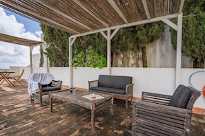 An outdoor patio with wooden furniture, a table, and a covered seating area. - Holiday Home 'Lua' with Sea View, Shared Pool and Wi-Fi (Aljezur)