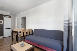 Un espace de vie compact comprenant un canapé, une table à manger, des chaises, un petit coin cuisine et une porte-fenêtre coulissante.