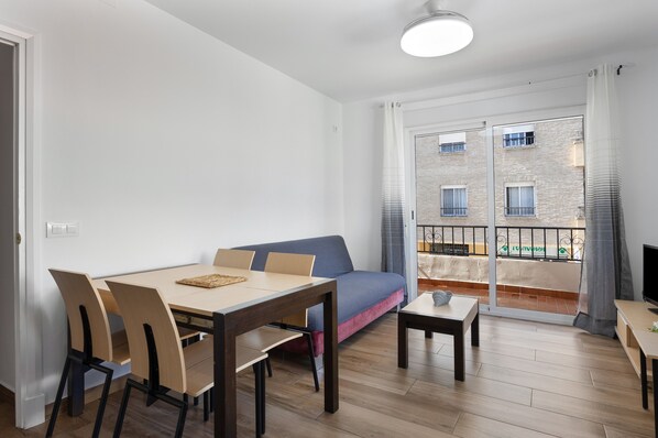 Una sala de estar moderna con una mesa de comedor, sillas, un sofá, un televisor y un balcón con barandilla.